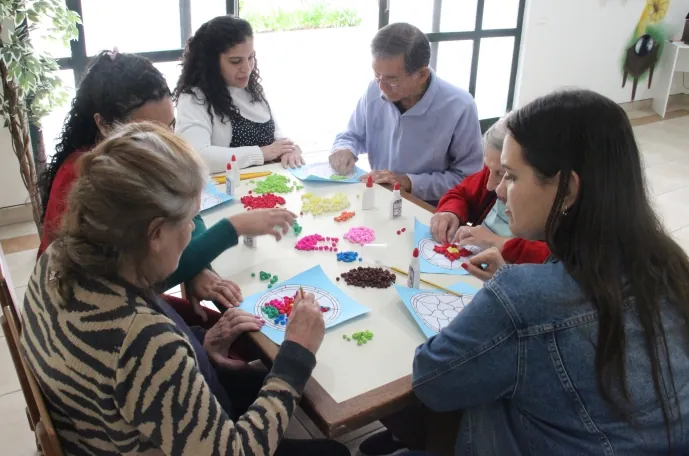 Moradores do Residencial Garden Ville em atividade de artesanato com mandalas de bolinhas coloridas, acompanhados pela equipe