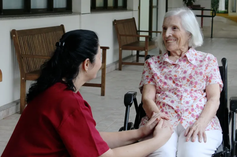 Cuidadora do Residencial Garden Ville conversa de mãos dadas com uma moradora sorridente na varanda do residencial