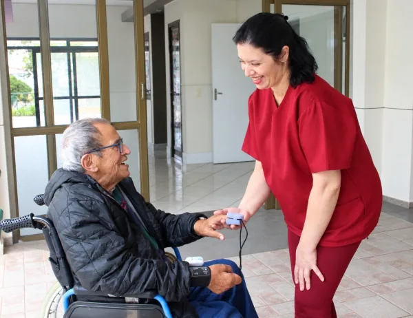 Cuidadora atende idoso em cadeira de rodas no Residencial Garden Ville